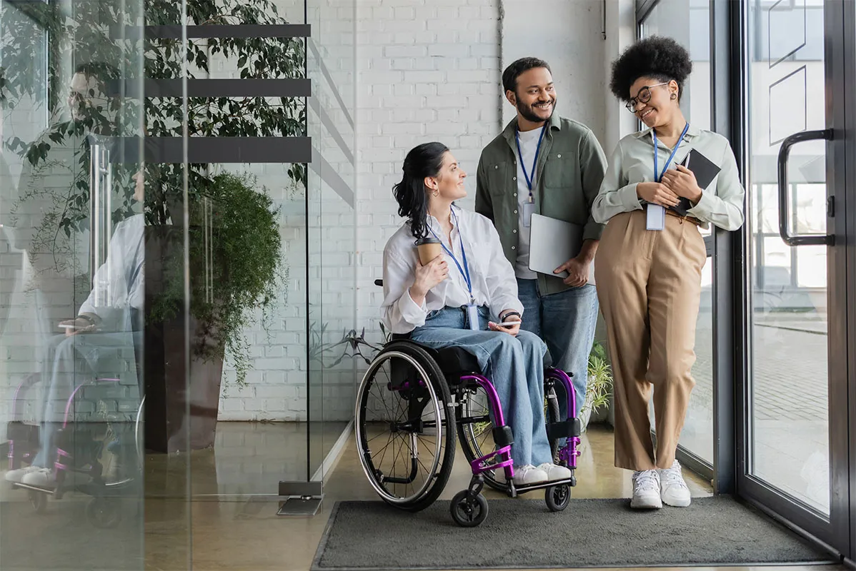 A woman in a wheelchair holding a coffee and talking to two people