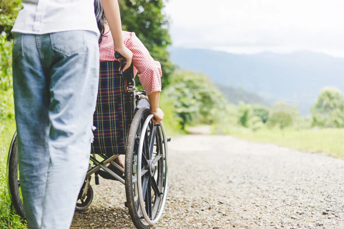 woman in wheelchair and care helper walking